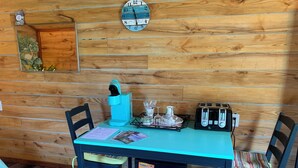 Interior de una cabaña de madera con una mesa, sillas, un reloj, un tostador y un refrigerador.