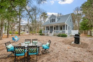 Une maison avec un porche, une table à manger avec des chaises et un barbecue dans le jardin.