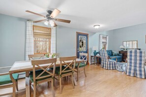 Un coin repas avec une table et des chaises en bois, un ventilateur de plafond et une vue sur le salon.