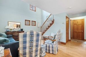 A living room with a staircase, a blue sofa, two plaid armchairs, a wooden coffee table, and a wooden door.