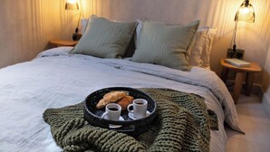A neatly made bed with a tray of croissants and coffee cups, a green knitted blanket, and two bedside lamps.