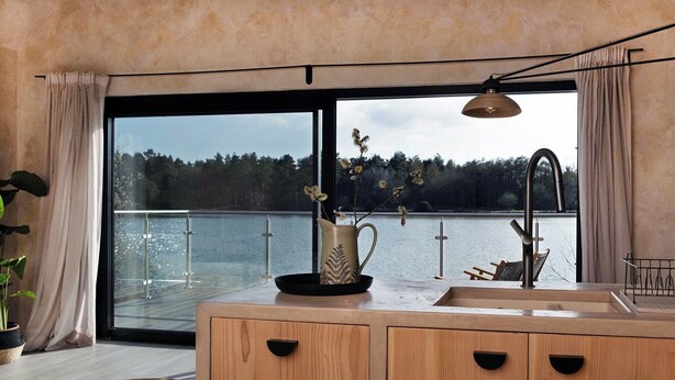 A modern kitchen with wooden cabinets, a sink, and a view of a lake through large glass doors.