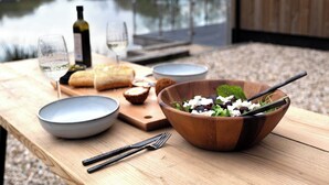 A wooden table with a salad bowl, wine glasses, and a bottle of wine.