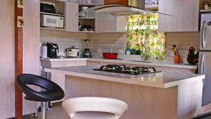 A modern kitchen with a central island, two bar stools, a microwave, a stove, and a large window with a green curtain.