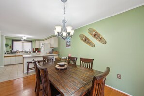 A dining area with a wooden table and chairs, a chandelier, and a kitchen in the background. - Wood Lot 28C - Retreat Near Recreation Center 2 Bedroom Townhouse by The Summit at Gore Mountain (North Creek)
