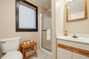 A bathroom with a toilet, a shower, a sink, a mirror, and a window with a blind. - Wood Lot 28C - Retreat Near Recreation Center 2 Bedroom Townhouse by The Summit at Gore Mountain (North Creek)