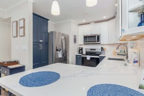 A modern kitchen with white cabinets, stainless steel appliances, and blue decorative mats on the island. - Bayside Condo with Sunset Pool (Ocean City)