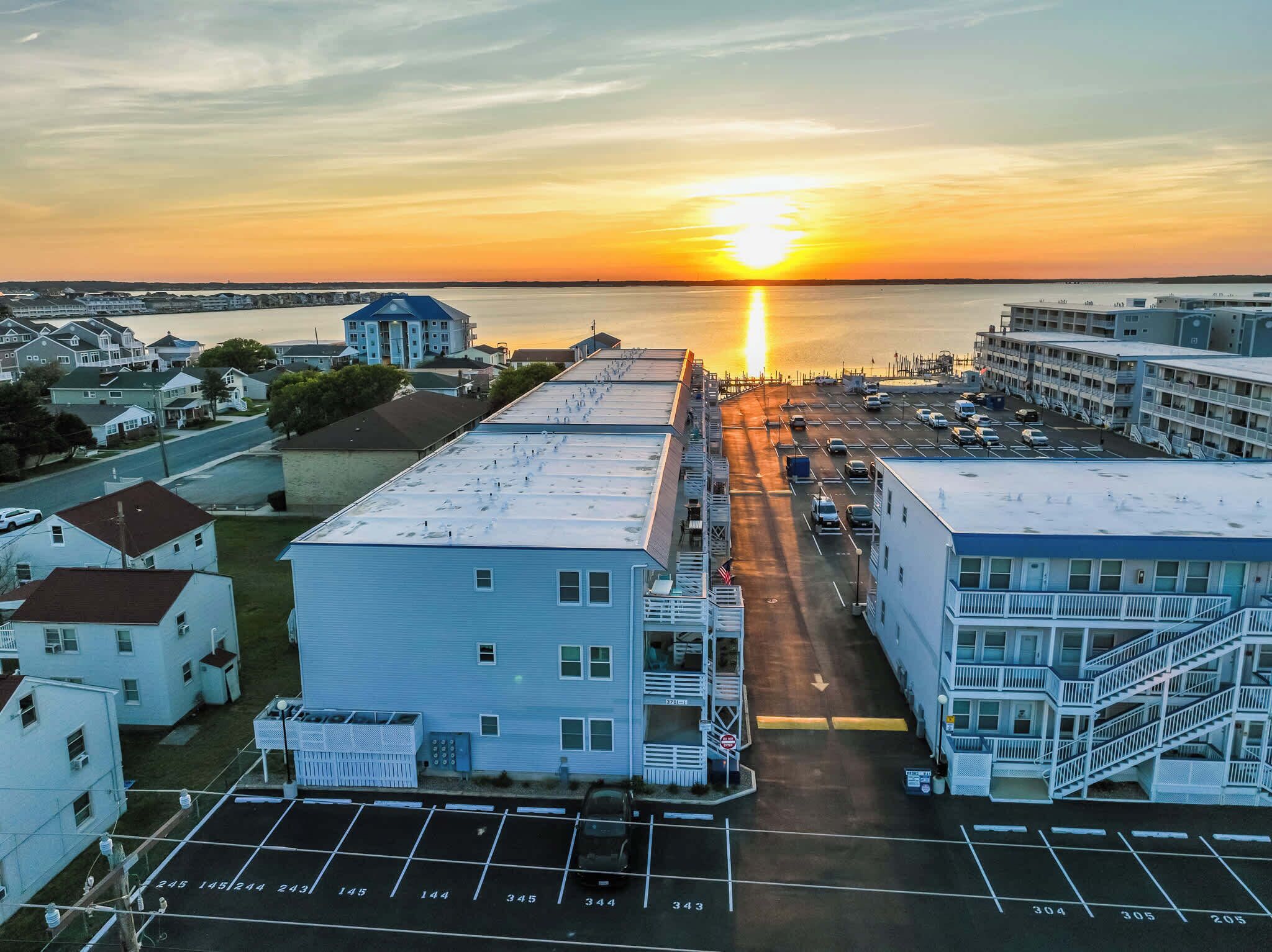 A parking lot with numbered parking spaces, a building with a blue roof, and a sunset over a body of water.