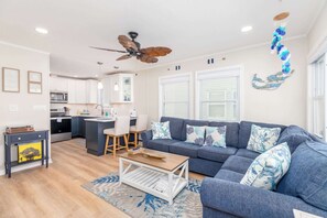 A modern living room with a blue sofa, wooden coffee table, and a ceiling fan. - Bayside Condo with Sunset Pool (Ocean City)