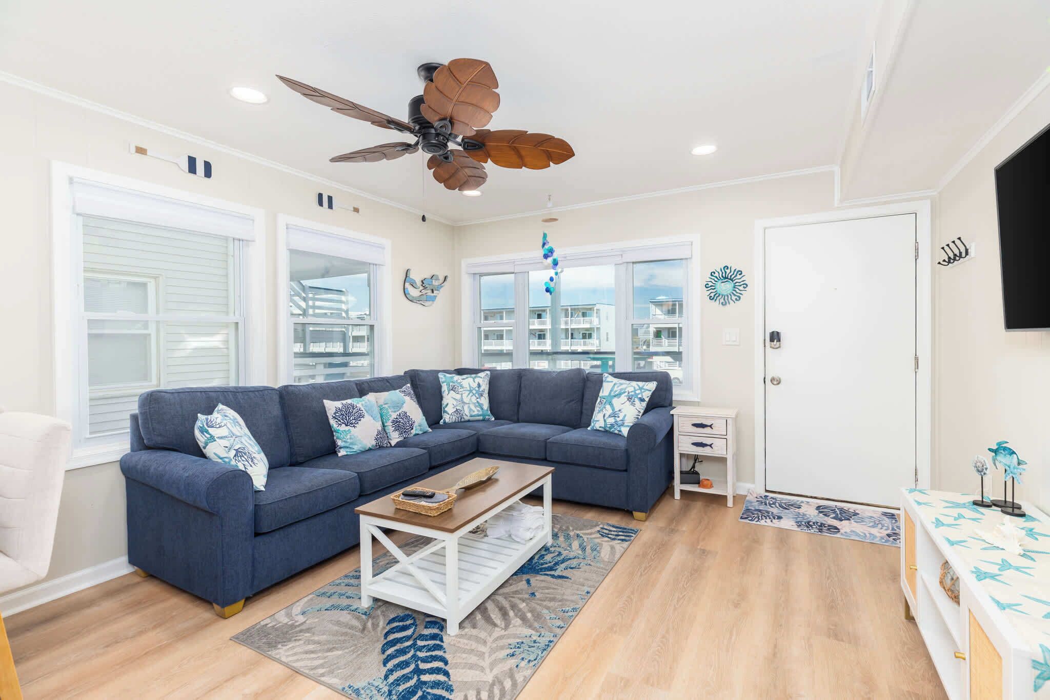 A living room with a sectional sofa, a ceiling fan, a coffee table, and a view of the city.