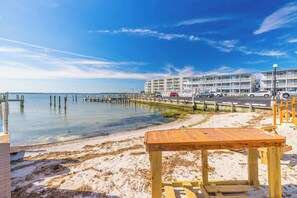 A beachside hotel with a wooden bench, a pier extending into the water, and a row of cars parked along the road. - Bayside Condo with Sunset Pool (Ocean City)