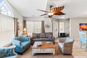 Ein Wohnzimmer mit Deckenventilator, einer Couch, einem Couchtisch und einem Korbstuhl.