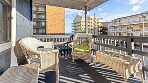 Un balcón con mobiliario de mimbre, una mesa de vidrio y vistas a un edificio costero.