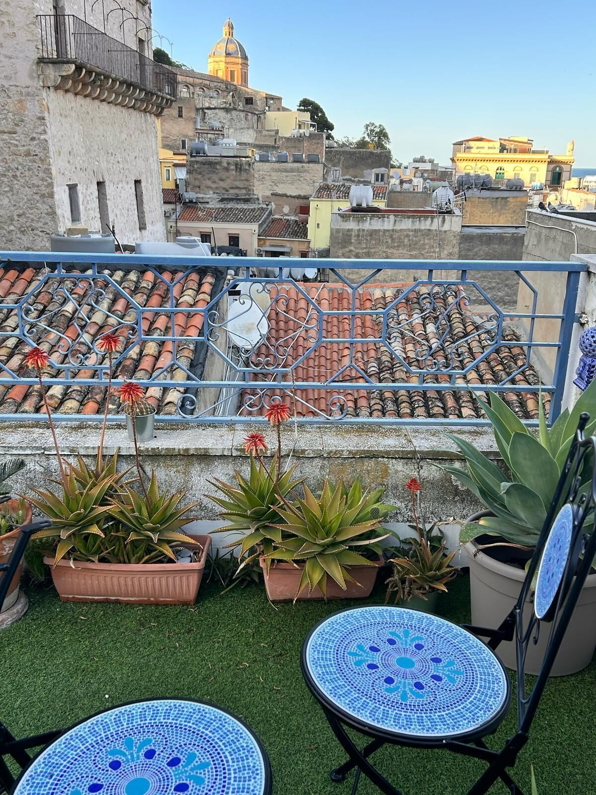 Una terraza en la azotea con baldosas de terracota, plantas en macetas y mesas de mosaico azul.