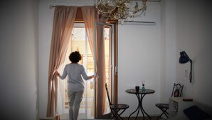 A room with a bed, a small table with a chair, a chandelier, and a window with curtains. - Casa Di Sylwia (Termini Imerese)