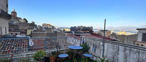 Una terrazza panoramica sul tetto con prato artificiale verde, piante in vaso, arredi da esterno e una vista aperta sulla città.