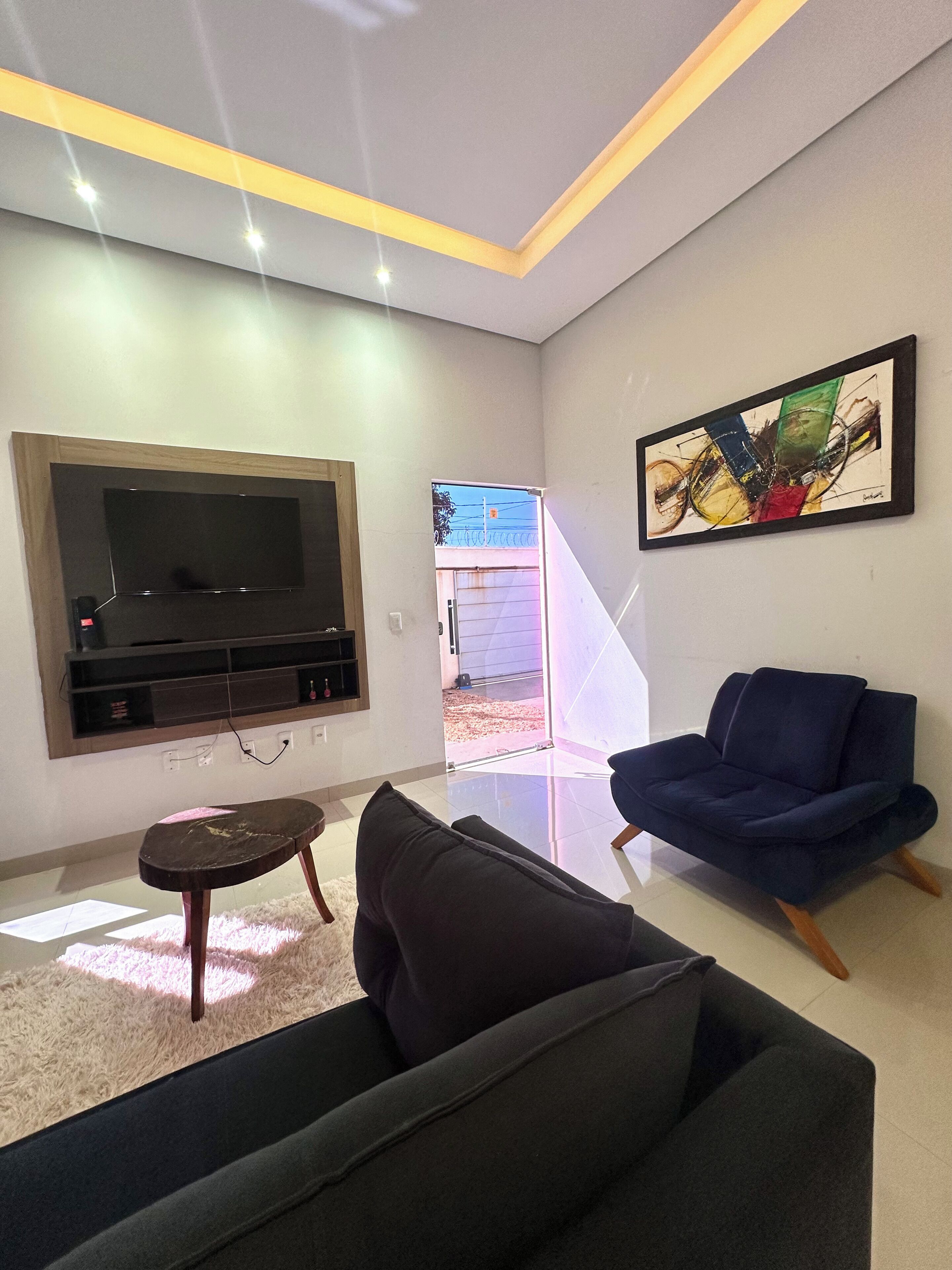 Un salon moderne avec un téléviseur à écran plat, un canapé bleu et un tableau accroché au mur.