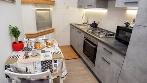 Eine kleine Küche mit Gasherd, Backofen und Mikrowelle. Ein Esstisch mit gemustertem Tischläufer und einem Blumentopf.