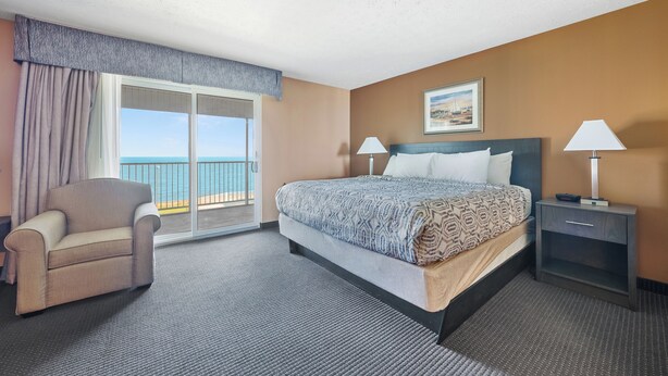 A hotel room with a bed, a chair, a nightstand, and a view of the ocean through a sliding door. - Hotel Suite Walking Distance to Downtown Put in Bay (Put-in-Bay)