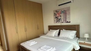 A bedroom with a wooden bed, white linens, a nightstand, a wall-mounted air conditioner, and a large wardrobe. - Aqua Luxe Ayia Napa Protaras Villa With Sea View (Paralimni)
