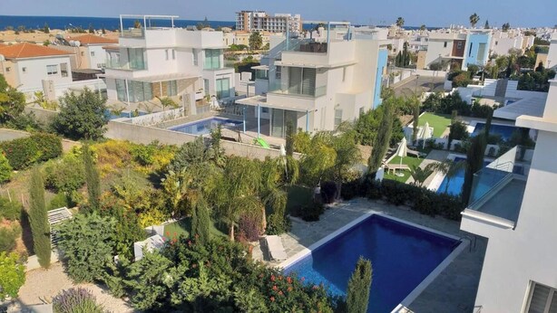 A modern residential area with a large swimming pool surrounded by lush greenery and a clear view of the sea. - Aqua Luxe Ayia Napa Protaras Villa With Sea View (Paralimni)