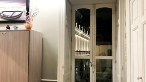 A room with a wooden cabinet, a small table with a lamp, and a glass door leading to a balcony with railings. - YourHome - Chiara's Apartment Sorrento 3 (Piano di Sorrento)