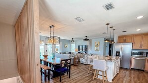 A modern kitchen with wooden flooring, a dining area with a bench, and a bar area with stools. - 7 Seas Ocean Breeze Sleeps Kitchens St George Island Pet Friendly Family (Eastpoint)