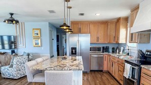 A modern kitchen with a marble island, wooden cabinets, stainless steel appliances, and a dining area with a sofa and chairs. - 7 Seas Ocean Breeze Sleeps Kitchens St George Island Pet Friendly Family (Eastpoint)