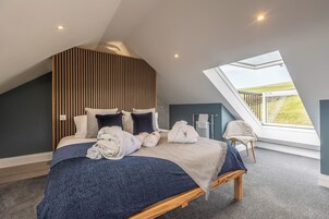 A bedroom with a sloped ceiling, a skylight, a bed with towels, a bench, and a view of the outdoors.