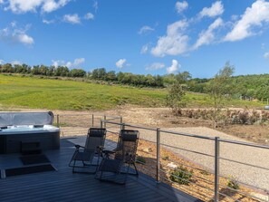 Terraza con mobiliario exterior y jacuzzi, con vistas a un campo cubierto de hierba y árboles.