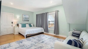 Een slaapkamer met een bed, een nachtkastje, een raam met gordijnen, uitzicht op buiten en een witte deur.