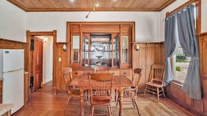 A wooden dining room with a large table and chairs, a built-in wooden cabinet with glass doors, and a wooden ceiling with exposed beams. - Franklin Manor at Grand Harbor 200-1 (Grand Haven)