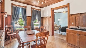 A dining area with a wooden table and chairs, a kitchen with wooden cabinets, and a view of the outdoors. - Franklin Manor at Grand Harbor 200-1 (Grand Haven)