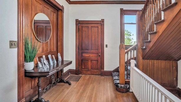 A wooden staircase with a white railing, a wooden door with a mirror above it, and a bench with magazines. - Franklin Manor at Grand Harbor 200-1 (Grand Haven)