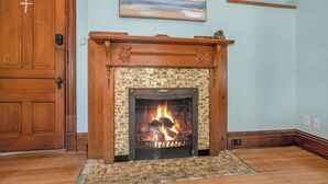 A fireplace with a brick surround and a wooden mantel, set in a room with light blue walls and wooden flooring. - Franklin Manor at Grand Harbor 200-1 (Grand Haven)