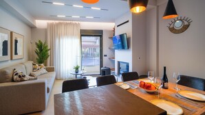 A modern living room with a sofa, dining table set for two, and a TV mounted on the wall. - Veneto Luxury Residence with pool in Venerato, Crete (Neo Venerato)