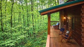 Una cabaña de madera con terraza, rodeada de un bosque denso.