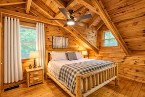 Une chambre confortable, aménagée dans un chalet en bois, avec un lit, des tables de chevet, un ventilateur de plafond et des fenêtres.