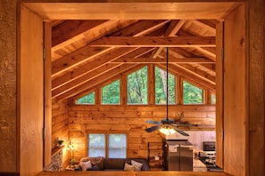 L’intérieur d’une cabane en rondins, avec un plafond incliné, un coin repas et un espace salon confortable doté d’une cheminée.