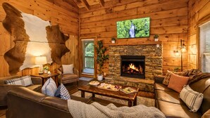 Un acogedor interior de cabaña de madera con chimenea de piedra, sofás de cuero y un televisor montado en la pared.