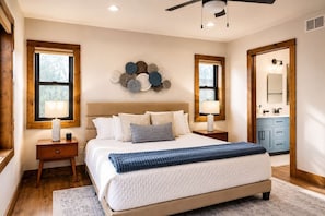 A bedroom with a large bed, two bedside tables, a ceiling fan, and a bathroom visible through an open door.