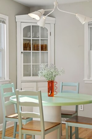 A dining area with a round table, four chairs, a vase with flowers, and a cabinet with glass doors. - Steps to downtown/ close to the River/ comfy beds (Minneapolis)