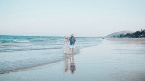 A beach scene with a couple standing on the shore, a calm sea, and a distant hill.
