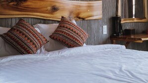 A bed with white linens and two patterned pillows, a wooden headboard, a wall-mounted light fixture, and a mirror on the wall.