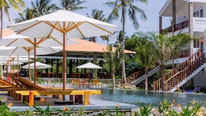 A poolside area with lounge chairs and umbrellas, a staircase leading to a building, and palm trees in the background.