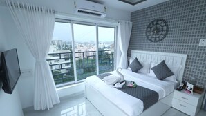 Une chambre d’hôtel moderne avec un grand lit, une table de chevet, une télévision et une vue sur la ville grâce à une grande fenêtre.