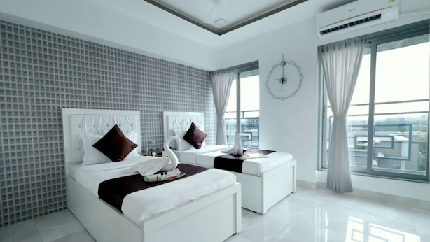 Une chambre d’hôtel moderne avec deux lits, une grande fenêtre donnant sur la ville et un mur recouvert de carreaux.