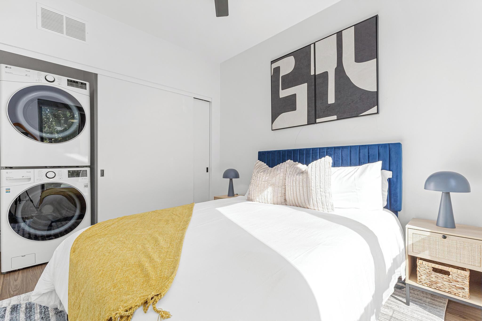 Un dormitorio moderno con una cama, una lavadora y un cuadro abstracto grande en la pared.
