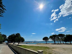 A coastal walkway with a clear view of the sea, trees, and distant boats. - Apartman Dalma  (Crikvenica)