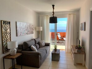 Relax in this stylish living room with a sofa, side table, and ocean views from the large window and balcony.